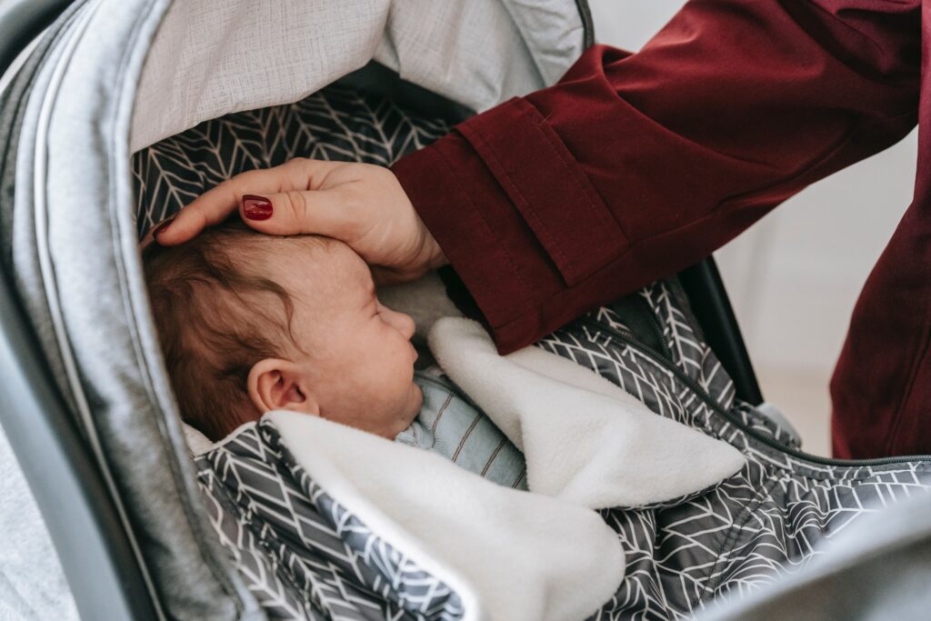 Person touching babies head in car seat